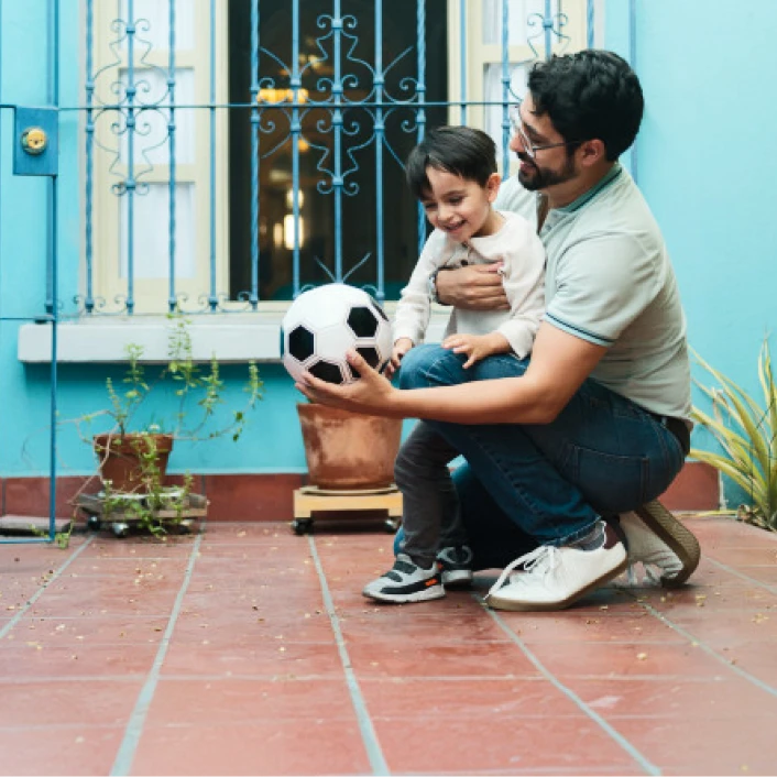 Persona adulta compartiendo tiempo con un menor en el patio de una vivienda, reflejando bienestar familiar y protección del hogar.