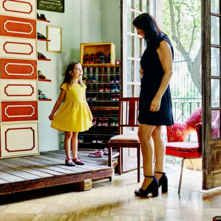 Persona adulta en una tienda, con su hija dentro de una tienda de zapatos, reflejando bienestar familiar, protección y diversión al momento de probarse productos de calzado.