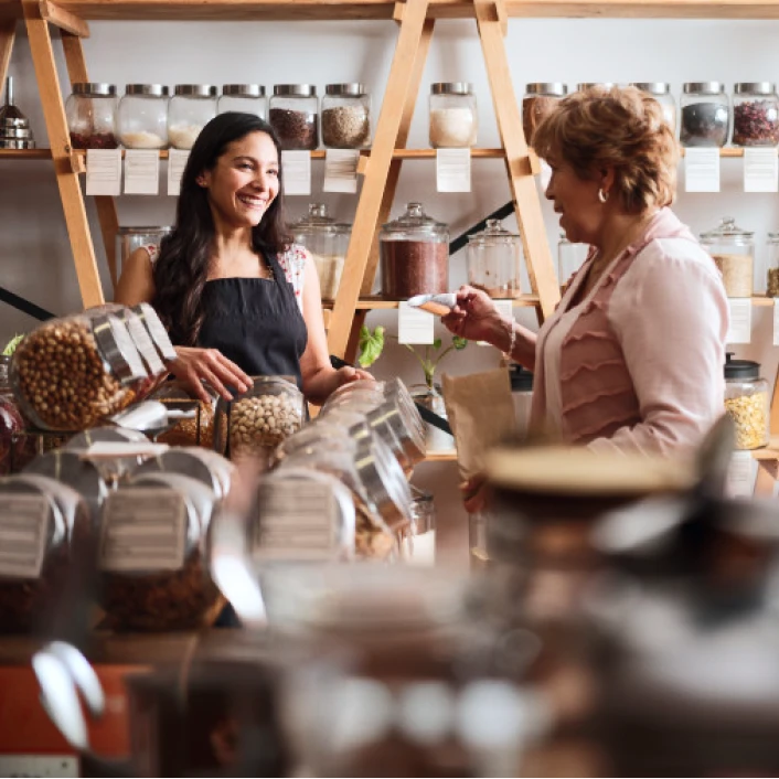 Persona atendiendo a una clienta en un comercio local, realizando una compra y promoviendo el crecimiento de pequeños negocios.