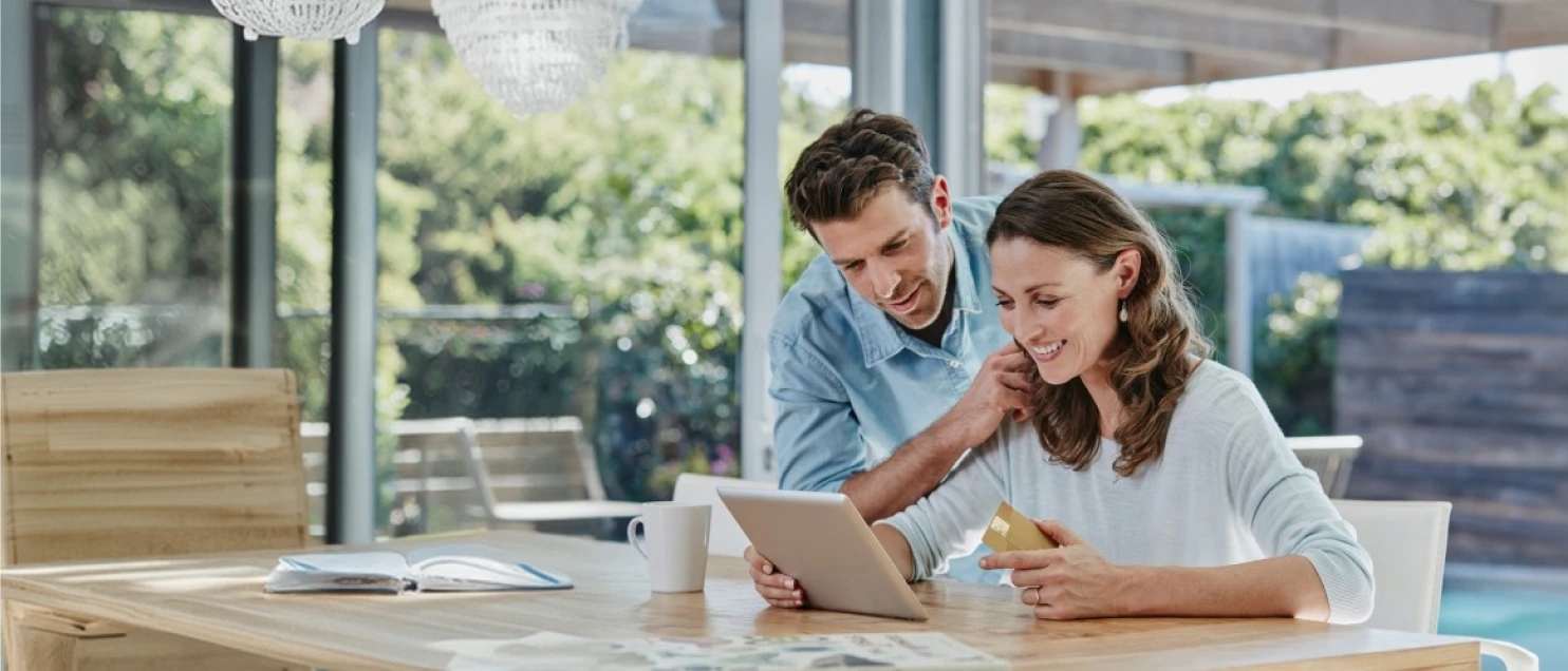 Pareja revisando información financiera desde una tablet y una tarjeta bancaria para comparar opciones y tomar decisiones de compra informadas.