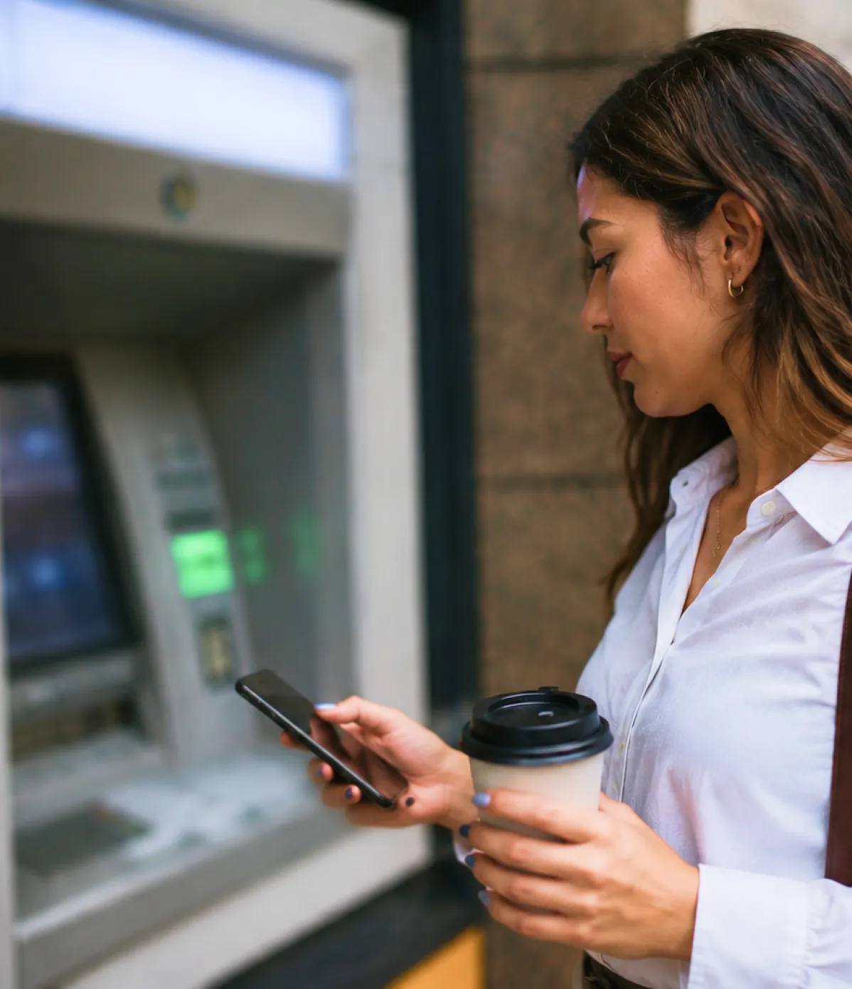Persona utilizando un teléfono móvil frente a un cajero automático, realizando operaciones bancarias y gestionando servicios financieros digitales.