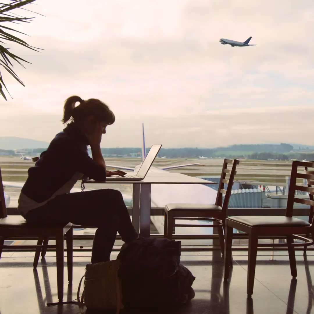 Persona trabajando con una computadora portátil en una terminal aérea, preparándose para un viaje mientras espera su próximo vuelo.