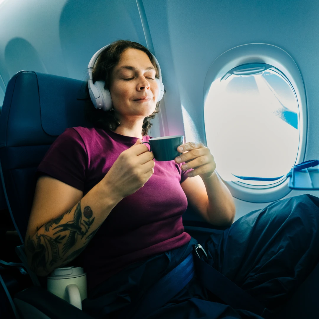 Persona descansando durante un vuelo mientras disfruta una bebida, reflejando comodidad, tranquilidad y bienestar durante el viaje.