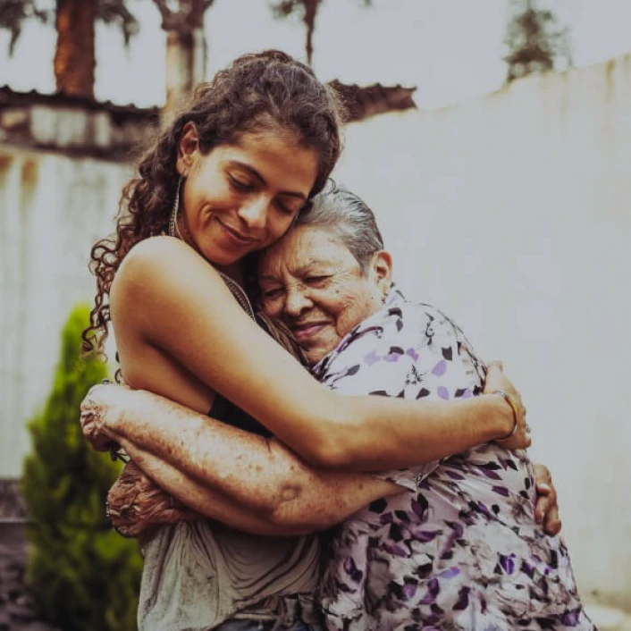 Persona adulta abrazando a una persona mayor, reflejando cuidado, protección, acompañamiento y bienestar familiar entre generaciones.
