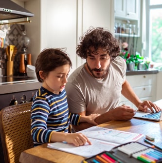 Un papá revisando con su hijo su tarea, sentados en la mesa de la cocina.