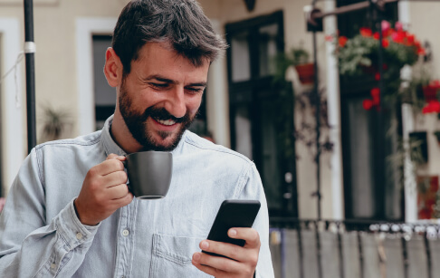 Hombre sosteniendo una taza de café, sonriendo mientras ve la app Banamex en su celular.