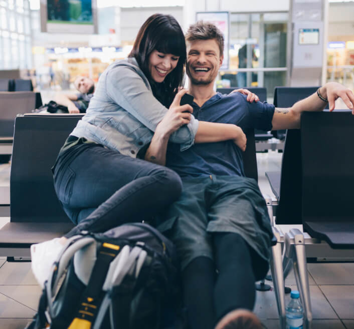 Pareja feliz sentada en una sala de espera de un aeropuerto junto a su mochila de viaje.