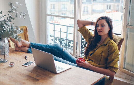 Mujer sentada frente a su escritorio con los pies arriba, mirando su laptop.