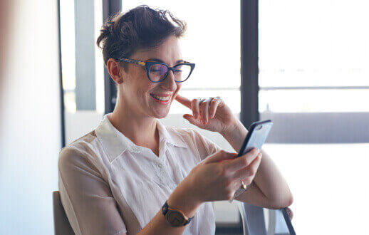Mujer de cabello corto y lentes sonriendo mientras ve sus ahorros en la app Banamex en su celular.