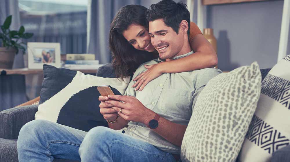 Una pareja sonríe mientras ven un celular en la sala.