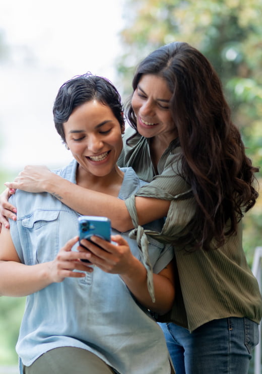 Un par de amigas abrazadas mientras una sostiene su celular.