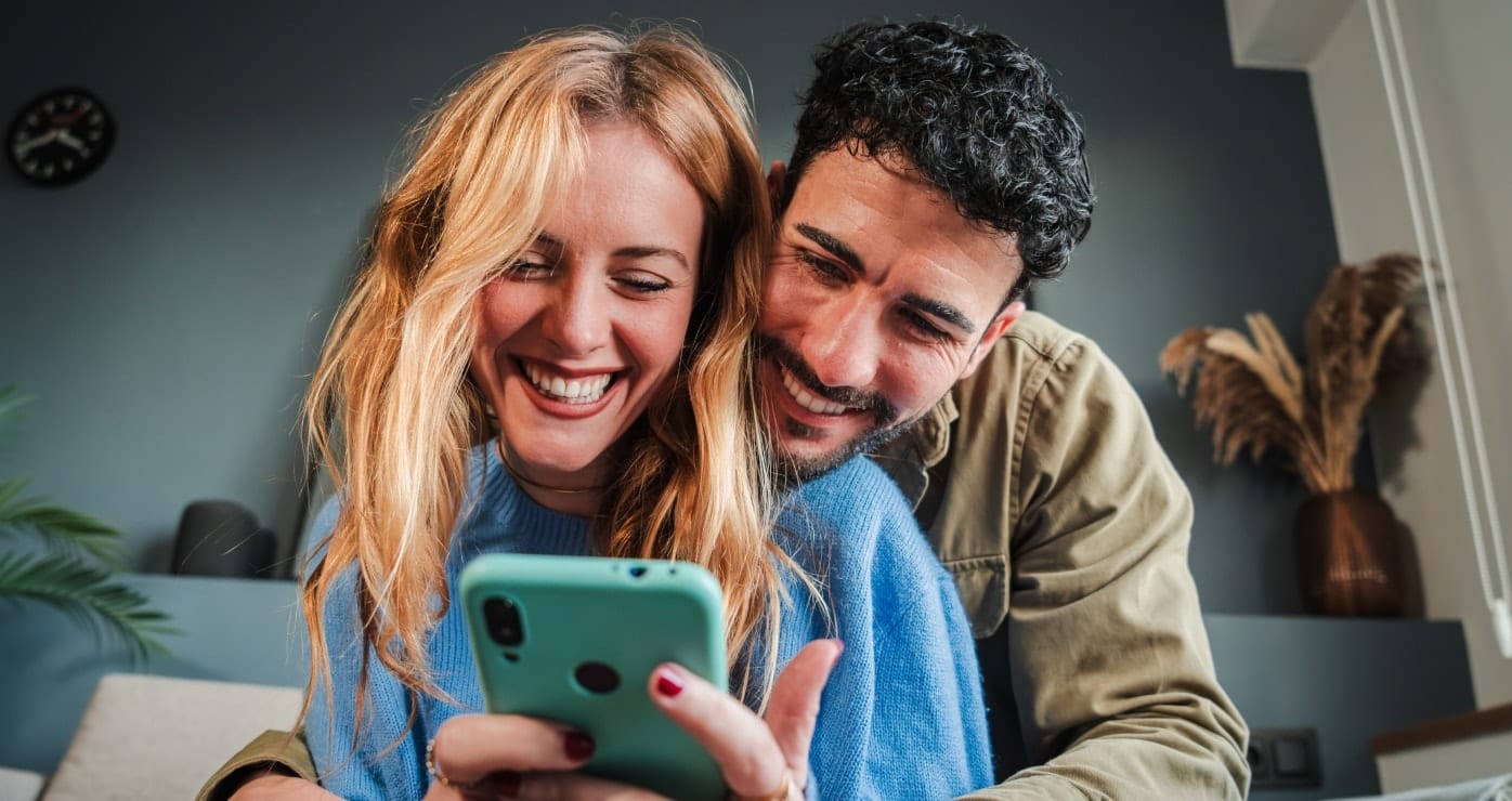 Una pareja abrazada mientras revisan su aplicación bancaria desde el celular con funda verde de ella.