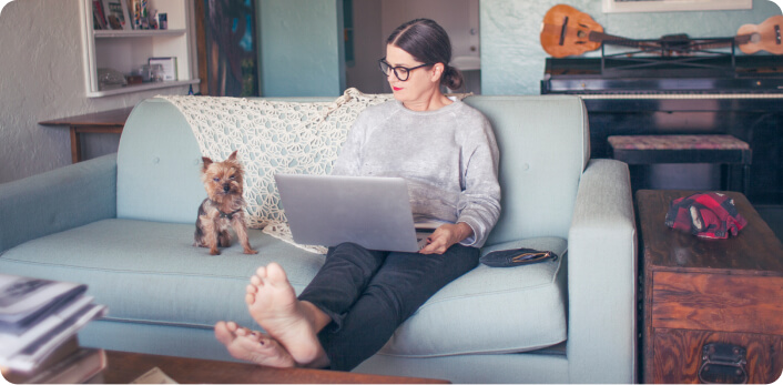 Una mujer trabaja con su laptop en la sala, acompañada de su perro.