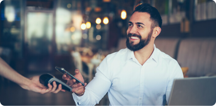 Un hombre sonriendo y pagando la cuenta de un restaurante con su celular.