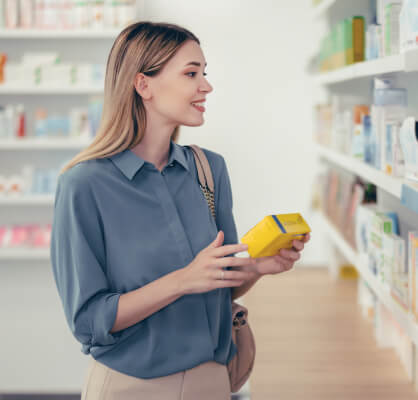 Una mujer sonriendo sosteniendo una caja de medicamento en una farmacia.