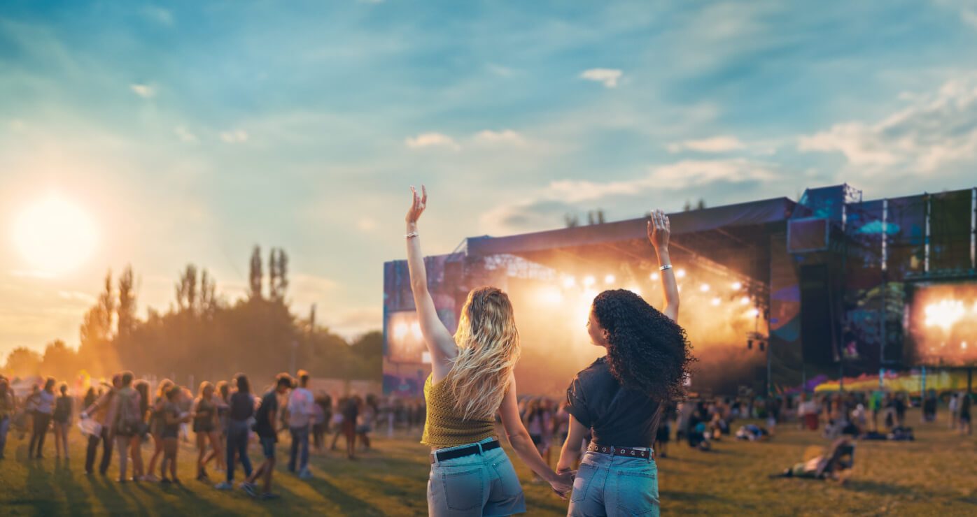 Dos amigas tomadas de la mano, disfrutando un concierto al aire libre con las manos levantadas.