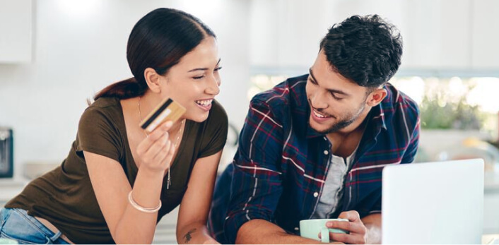 Una pareja sentada en una mesa mientras hacen una compra en línea con una tarjeta de crédito.