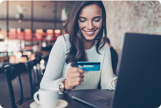Una mujer sonriendo realiza una compra en línea en su laptop mientras toma un café.
