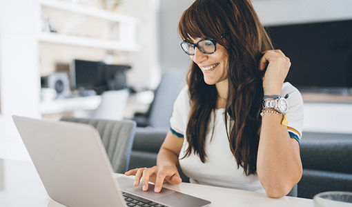 Una mujer sentada en una mesa utilizando una laptop y sonriendo.