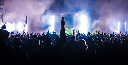 Multitud disfrutando de un concierto en vivo con luces brillantes en el escenario, levantando las manos.