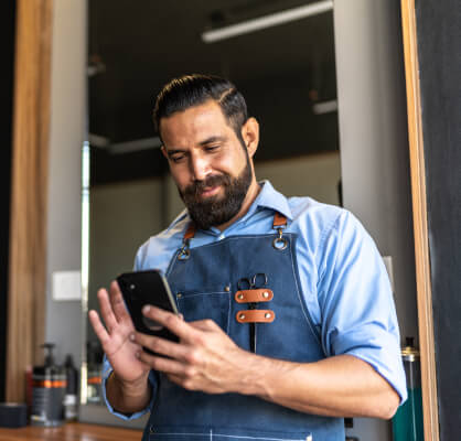Hombre con babero de barbería revisando el depósito de su nómina en su app móvil.