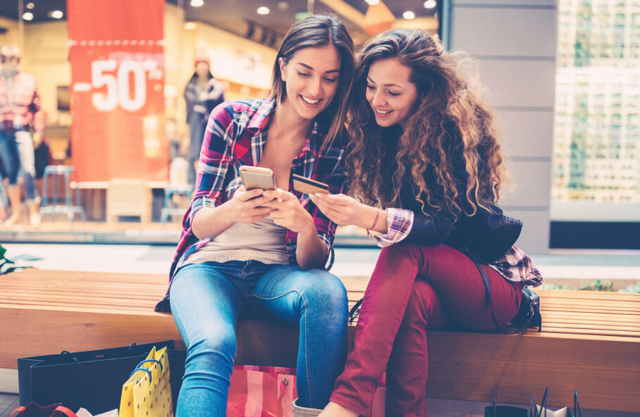 Un par de chicas en un centro comercial compartiendo su tarjeta en su app móvil.