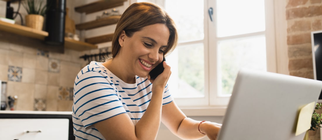 Una mujer sentada frente a su computadora, hablando por teléfono y revisando sus finanzas.