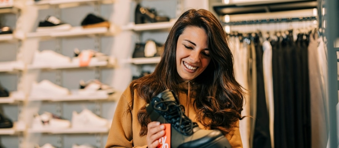 Una mujer tomando una bota y pensando aprovechar las ofertas del Buen Fin con su tarjeta de débito. 