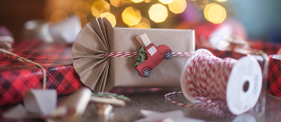 Un regalo de reyes magos, envuelto en papel craft con un carro pegado delante del arbol de navidad.