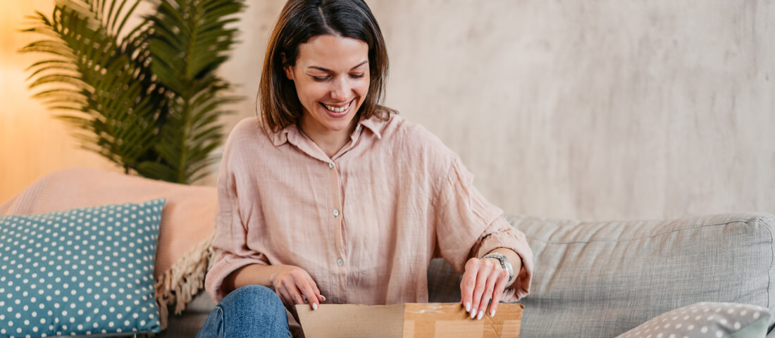 Una mujer sentada abriendo un paquete de cartón en casa.