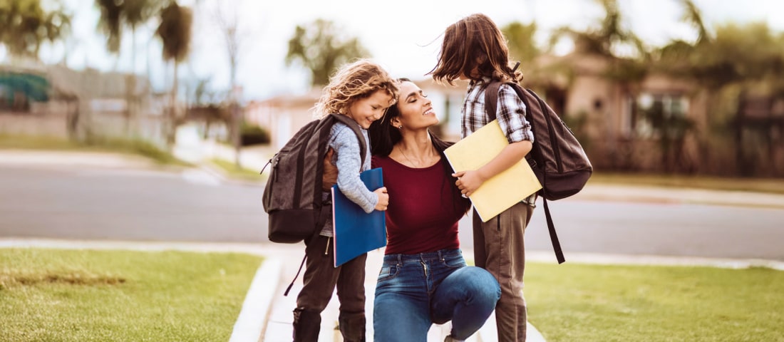 Madre despidiendo a sus hijos con mochilas y cuadernos en el regreso a clases