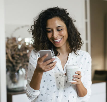 Emprendedora sonriendo con café y celular.